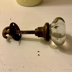 May include: A vintage glass doorknob with a brass base and a metal hook attached to a metal plate.