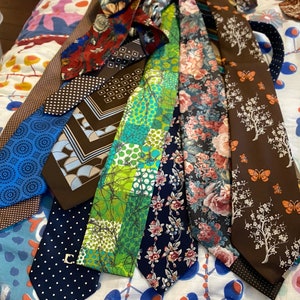 May include: A collection of 10 patterned neckties in various colors and designs, including floral, geometric, and abstract patterns. The ties are arranged in a fan shape on a patterned fabric background.