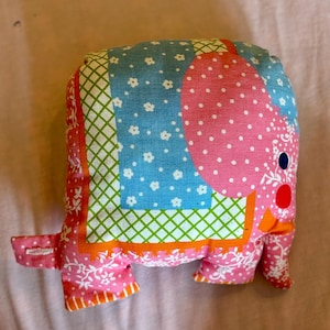 May include: A pink and blue patchwork elephant stuffed animal with white polka dots and floral patterns. The elephant has a green and orange patterned trunk and a red nose.