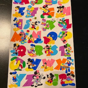 May include: A sheet of colorful alphabet stickers featuring Mickey Mouse and his friends. Each letter is decorated with a different character and activity, such as Mickey playing the guitar, Minnie riding a zebra, and Donald playing the xylophone.