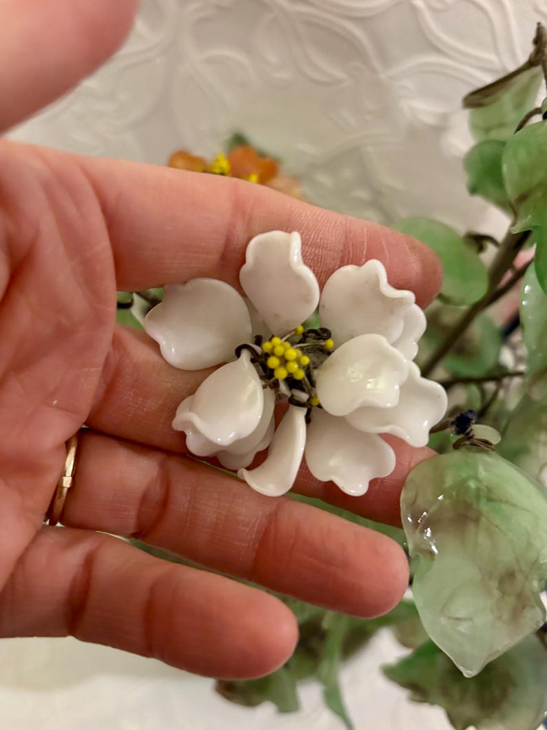May include: A close-up of a white flower with yellow and black accents in the center. The flower has multiple petals and is part of a larger floral arrangement. Green leaves are also visible.