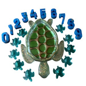 May include: A collection of resin art pieces featuring a large green turtle with a gold border, surrounded by small teal turtles and blue number shapes from zero to nine. The turtle and numbers have glitter accents.