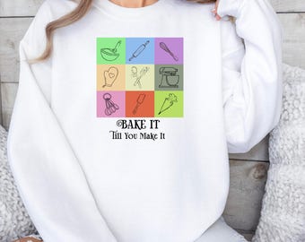 May include: White sweatshirt with a graphic of baking tools in colorful squares. The text "BAKE IT 'Till You Make It" is below the graphic.
