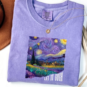 K&ouml;nnte beinhalten: Ein fliederfarbenes Comfort Colors T-Shirt mit einem Druck von Van Goghs "Sternennacht"-Gem&auml;lde. Das Kunstwerk zeigt wirbelnde Blau-, Lila- und Gelbt&ouml;ne mit dem Text "LET IT GOGH" in Wei&szlig;. Eine goldene Halskette liegt auf dem Shirt.