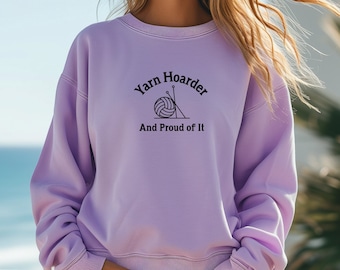 Op de afbeelding: Een lavendelkleurig sweatshirt met de tekst "Yarn Hoarder And Proud of It" en een afbeelding van een bol garen en breinaalden.