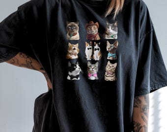 May include: Black t-shirt featuring a grid of nine cat portraits. Each cat is dressed in various outfits, including bow ties, a cowboy hat, and a bandana. The cats are in different colors and patterns.