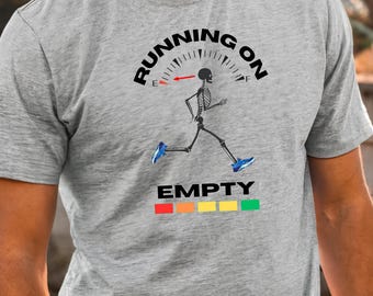 May include: A grey t-shirt featuring the text "RUNNING ON EMPTY" above a running skeleton graphic. The skeleton wears blue trainers. Below the text is a horizontal bar with coloured blocks.