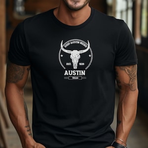 Puede incluir: Camiseta negra con un diseño gráfico blanco que presenta una calavera con cuernos y el texto "Keep Austin Weird" en un círculo con el texto "Est. 1839 Austin Texas".