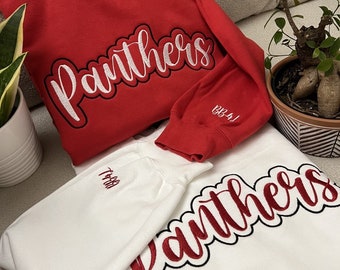 May include: Two sweatshirts, one red and one white, with the word "Panthers" embroidered in white on the red sweatshirt and red on the white sweatshirt. The red sweatshirt has the number "132-41" embroidered on the sleeve.