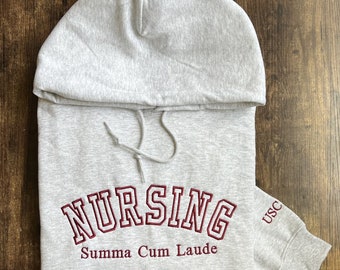 May include: Gray hooded sweatshirt with the words "Nursing Summa Cum Laude" embroidered in maroon on the front and "USC" embroidered in maroon on the sleeve.