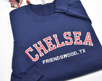 May include: Navy blue sweatshirt with white text that reads "CHELSEA FRIENDSWOOD, TX" in a red and white arched font.