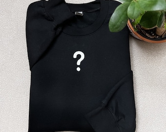 May include: Black sweatshirt with a white question mark on the front.