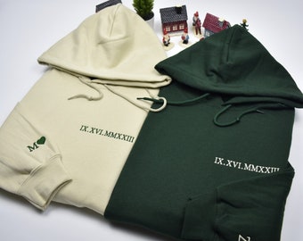 May include: Two hooded sweatshirts, one in cream and one in forest green, with embroidered hearts and roman numerals. The cream sweatshirt has an 'M' and the green sweatshirt has a 'Z'. The text on both sweatshirts reads 'IX.XVI.MMXXIII'.