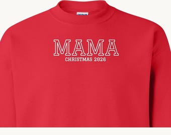 May include: A bright red crewneck sweatshirt featuring white block lettering that reads MAMA with the text CHRISTMAS 2026 printed in a smaller white font directly underneath the main word on the center of the chest.