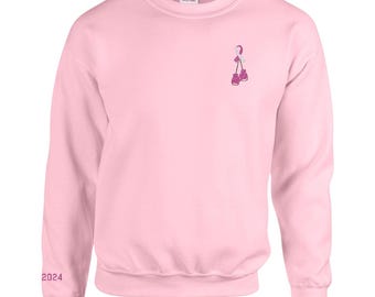 May include: A pink sweatshirt with a small embroidered design of ice skates on the front. The text "2024" is embroidered on the left sleeve.