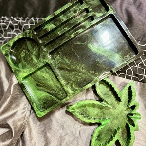 May include: A black and green resin rolling tray with a leaf design and multiple compartments. The tray is made of a marbled resin with a glossy finish.
