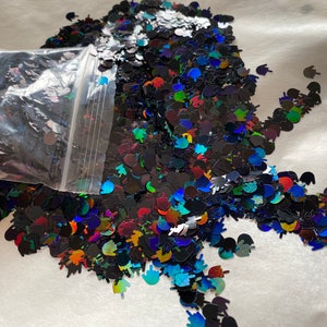 Op de afbeelding: Een zak met iriserende zwarte glitter met verschillende kleurrijke holografische vormen, waaronder kleine handgebaren.