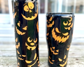 以下が含まれることがあります： オレンジ色のグリッターのジャック・オー・ランタンの顔が付いた、黒いハロウィーンをテーマにしたタンブラー2個。1つは背が高くストレートなタンブラー、もう1つは短く先細りのタンブラーです。どちらも光沢のある仕上がりです。