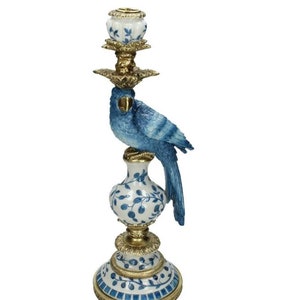 May include: A decorative candlestick with a blue bird perched on top. The candlestick has a white and blue floral design with gold accents. The bird is blue with detailed feathering. The base is round and ornate.