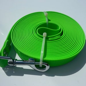 Op de afbeelding: Felgroene hondenriem opgerold en vastgezet met witte kabelbinders. De riem heeft een getextureerd oppervlak en een zilveren metalen sluiting. Ontworpen voor huisdiereigenaren.