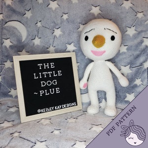Może przedstawiać: Wzór na szydełkowanie białego amigurumi psa o imieniu Plue. Wzór jest dostępny jako plik PDF do pobrania. Obraz przedstawia gotowego, uszydełkowanego Plue na szarym i białym kocu z tabliczką z napisem "The Little Dog ~ Plue @KelseyKayDesigns".