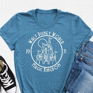 May include: A teal blue t-shirt with a white graphic of Cinderella's castle, the text "Walt Disney World", "1971", and "Magic Kingdom".