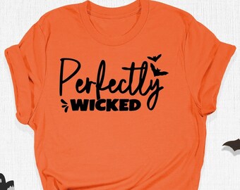 May include: Orange t-shirt with the phrase "Perfectly Wicked" in black script, decorated with bat and ghost cutouts. The shirt is a Halloween-themed apparel item.