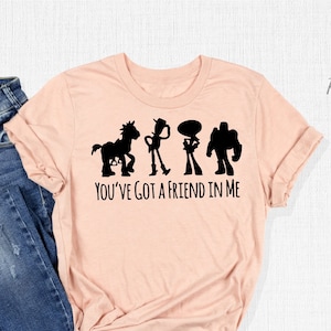 May include: A pink t-shirt featuring a black silhouette of the Toy Story characters Woody, Buzz Lightyear, and Bullseye, with the text "You've Got a Friend in Me".