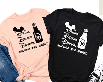 May include: Two t-shirts with a black and white graphic design of a beer bottle and Mickey Mouse ears with the text "Drink Drank Drunk Around the World".