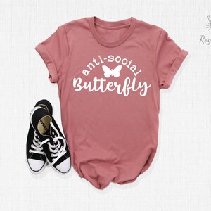 May include: A dusty rose t-shirt with the text "anti-social butterfly" in white lettering with a white butterfly graphic.
