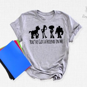 May include: Grey t-shirt featuring a black silhouette of the Toy Story characters Woody, Buzz Lightyear, Jessie, and Bullseye. The text "You've got a friend in me" is printed below the characters.