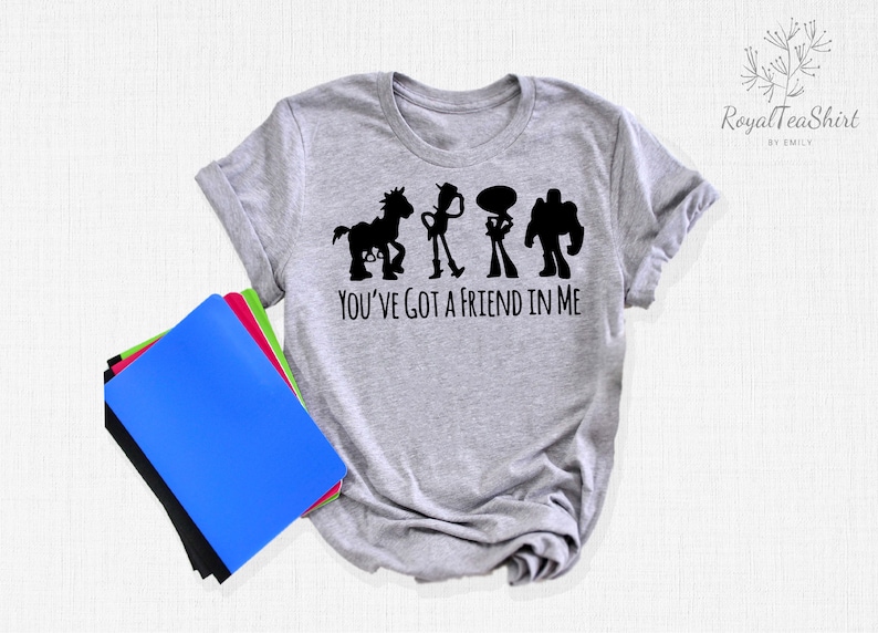 May include: Grey t-shirt featuring a black silhouette of the Toy Story characters Woody, Buzz Lightyear, Jessie, and Bullseye. The text "You've got a friend in me" is printed below the characters.