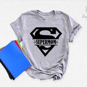 K&ouml;nnte beinhalten: Ein graues T-Shirt mit einem schwarzen Superman-Logo und dem Text "SUPERMOM" im Logo.