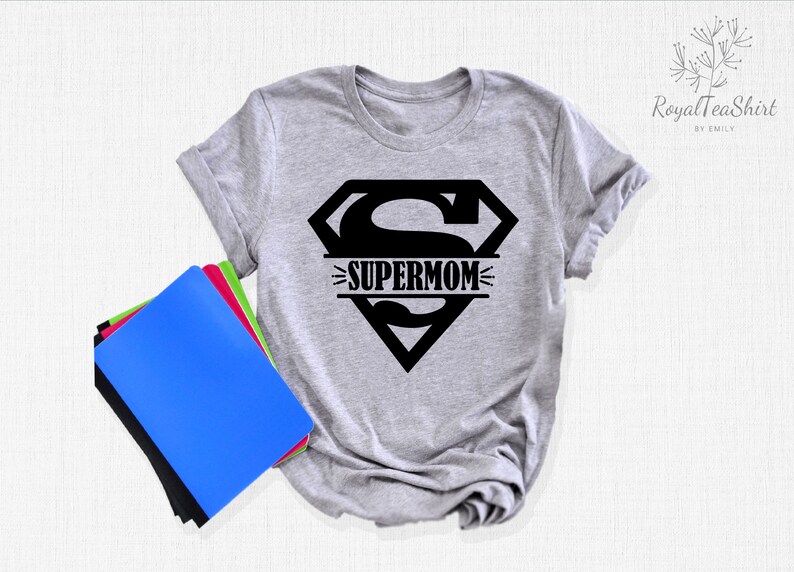 K&ouml;nnte beinhalten: Ein graues T-Shirt mit einem schwarzen Superman-Logo und dem Text "SUPERMOM" im Logo.