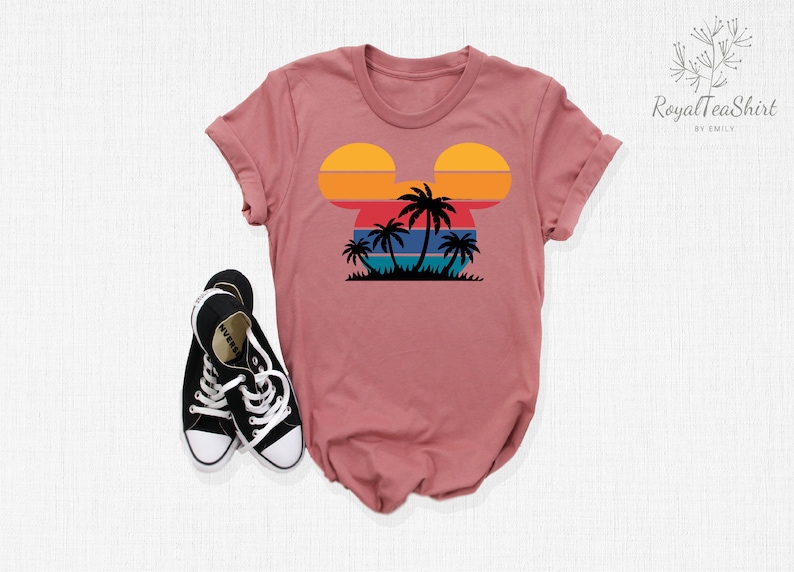 May include: A pink t-shirt with a retro sunset and palm trees in the shape of Mickey Mouse's head.
