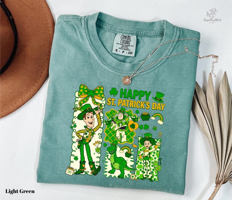 A light green t-shirt with a cartoon character and text printed on it, along with a brown hat and some leaves.