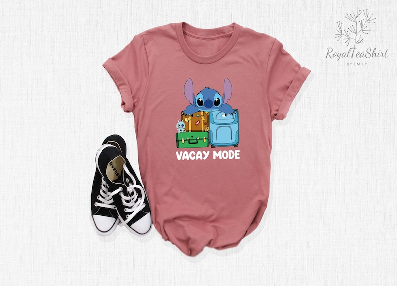 May include: A pink t-shirt with a blue Stitch character from Lilo & Stitch holding luggage. The text "Vacay Mode" is printed on the shirt.