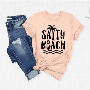 May include: A peach-colored t-shirt with a black palm tree and the text "SAPPY BEACH" in a playful font.