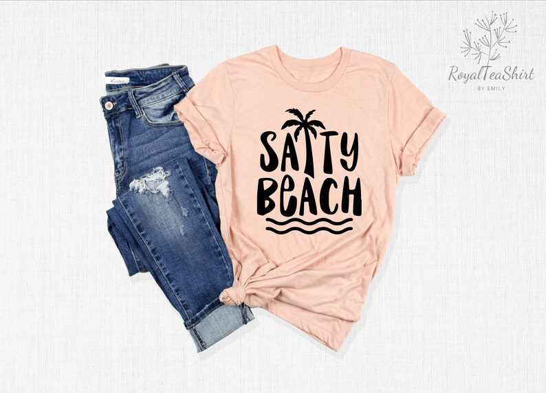 May include: A peach-colored t-shirt with a black palm tree and the text "SAPPY BEACH" in a playful font.
