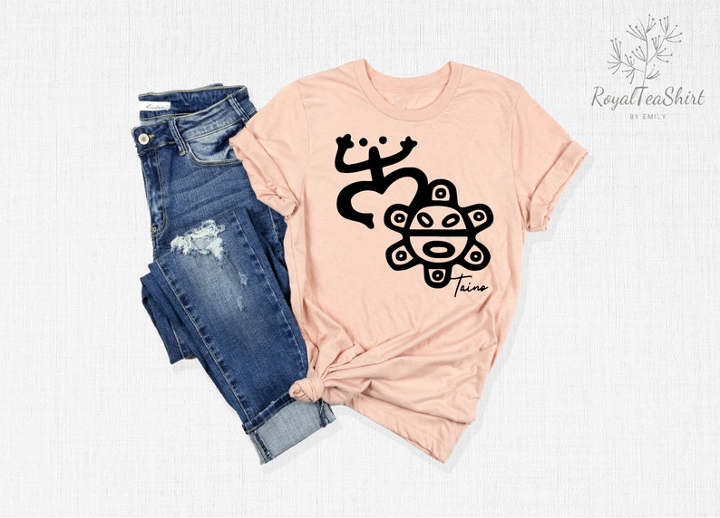 May include: A pink t-shirt with a black design of a frog and a sun with a face. The text "Taino" is below the design.