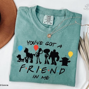 A light green t-shirt with a graphic design featuring silhouettes of characters from the animated film Toy Story, along with the text "You've got a friend in me" printed on it.