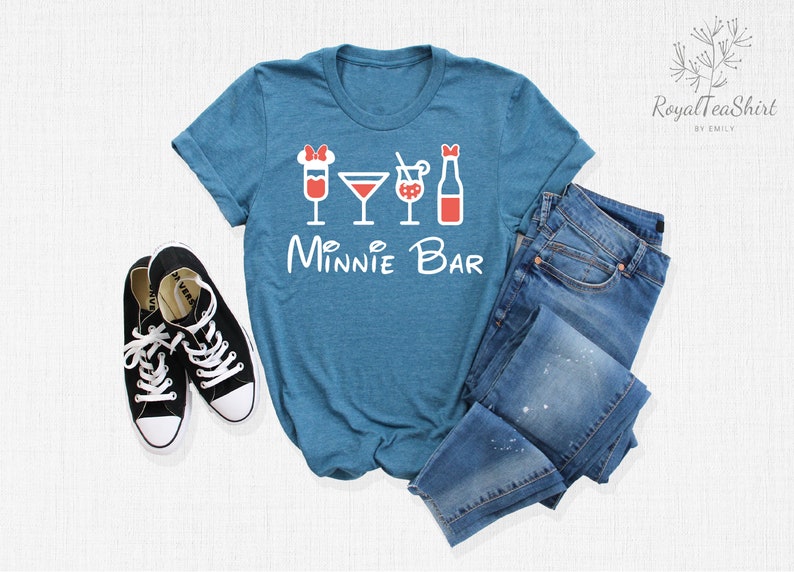 May include: A teal blue t-shirt with a white graphic of four drinks and the text "Minnie Bar". The t-shirt is laid out on a white surface with a pair of black sneakers and a pair of blue jeans.