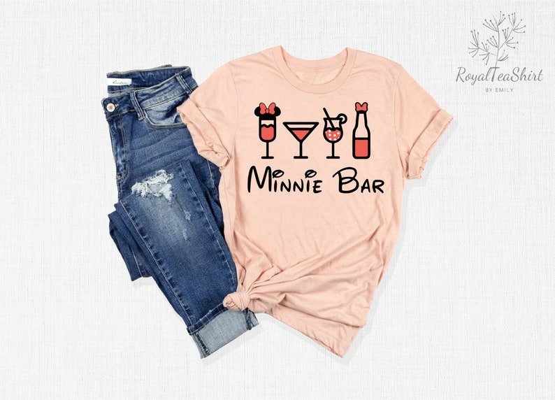 May include: A pink t-shirt with a black graphic of Minnie Mouse ears and four drinks, including a martini glass, a glass with a straw, a glass with a cherry, and a bottle. The text "Minnie Bar" is below the graphic.