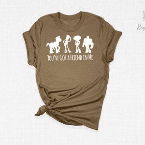 May include: A brown t-shirt featuring a white silhouette of the Toy Story characters Woody, Buzz Lightyear, Jessie, and Bullseye. The text "You've got a friend in me" is printed below the characters.