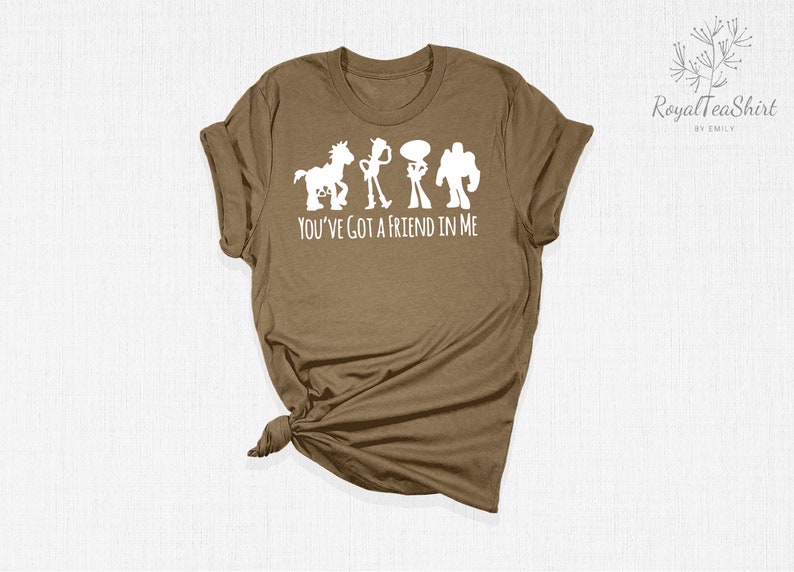 May include: A brown t-shirt featuring a white silhouette of the Toy Story characters Woody, Buzz Lightyear, Jessie, and Bullseye. The text "You've got a friend in me" is printed below the characters.