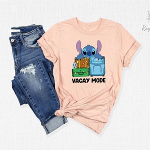 May include: A pink t-shirt with a blue cartoon character holding luggage and the text "Vacay Mode".