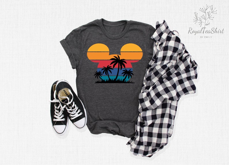 May include: A dark gray t-shirt with a retro sunset design in the shape of Mickey Mouse ears. The design features palm trees and a blue ocean.