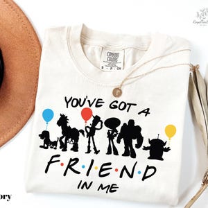 A white t-shirt with a graphic design featuring silhouettes of characters from the TV show Toy Story, along with the text "You've Got a Friend in Me".
