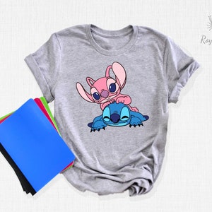 K&ouml;nnte beinhalten: Graues T-Shirt mit einem blauen und rosa Stitch- und Angel-Cartoon-Design. Das Design zeigt Angel auf Stitch.