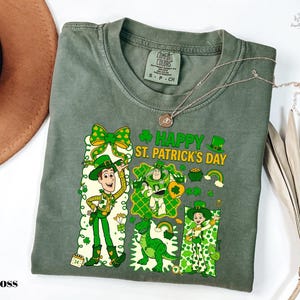 A green t-shirt with a cartoon character and text printed on it, along with a brown hat and some leaves.